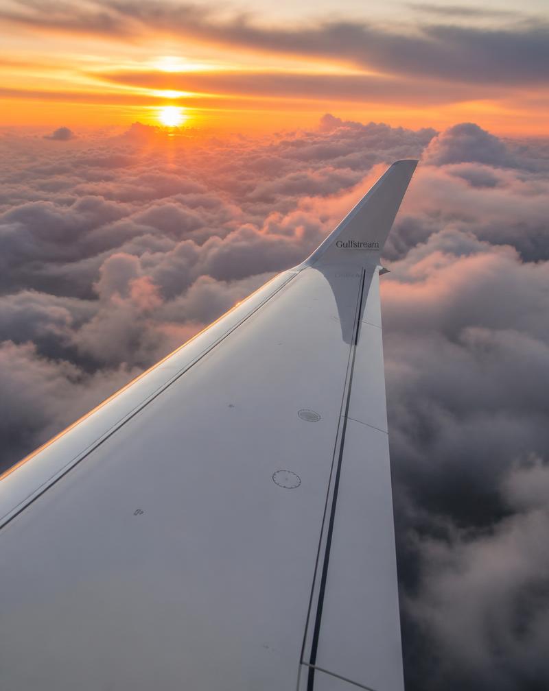 Private jet wing above clouds at sunset