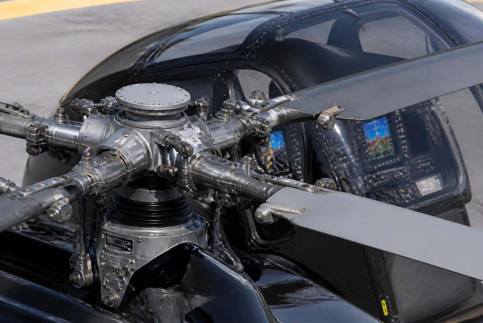 Close-up of a helicopter main rotor head and blades with the glass cockpit behind